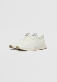 White knit athletic shoes with a textured pattern, a light-colored sole, and a grey tab on the heel. Low-cut design with laces for fastening.