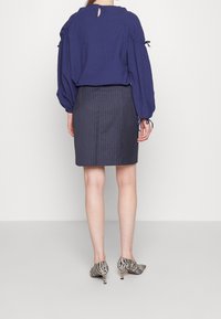 Blouse en maille navy avec des manches bouffantes, détail à trou clé au dos, associée à une jupe cintrée à rayures et des chaussures à rayures noir et blanc.