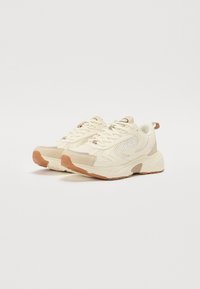 Zapatillas deportivas beige con superposiciones de malla y sintético, puntera redonda, cordones tonales y una suela de goma que presenta el logo de Fila.