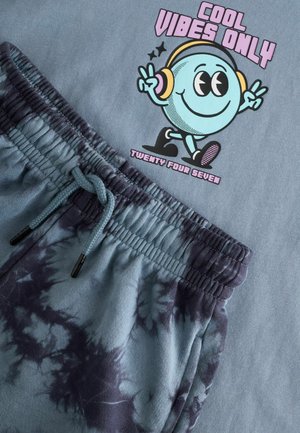 Light blue T-shirt featuring a colorful cartoon graphic and text. Blue tie-dye joggers with an elastic waistband and drawstring accent.