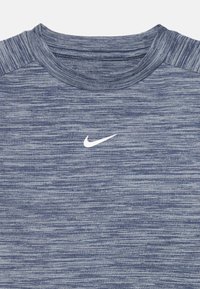 Pogled od blizu na plavi majico s kratkimi rokavi športnega kroja, z belim logotipom Nike swoosh v središču prsnega dela.