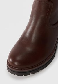 Bottine en cuir marron avec une finition lisse, bout arrondi et semelle en caoutchouc noir texturé. Dispose de panneaux latéraux élastiques pour un enfilage facile.
