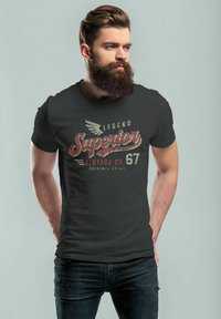 Schwarzes T-Shirt mit einem Vintage-Druck, der "Legend Superior Vintage Co. 67" in Rot, Creme und Grau zeigt. Enges Design, kurze Ärmel.