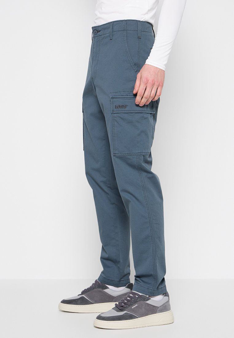 Cargo-Hosen in einem dunkelblauen Farbton, aus Baumwolle, mit Seitentaschen und einem Bund mit Gürtelschlaufen. Getragen mit grauen Sneakers.