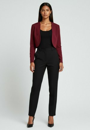 Blazer corto color bordeaux sopra una maglietta nera, abbinato a pantaloni neri su misura e tacchi neri. Tessuto liscio; design aderente con linee pulite.