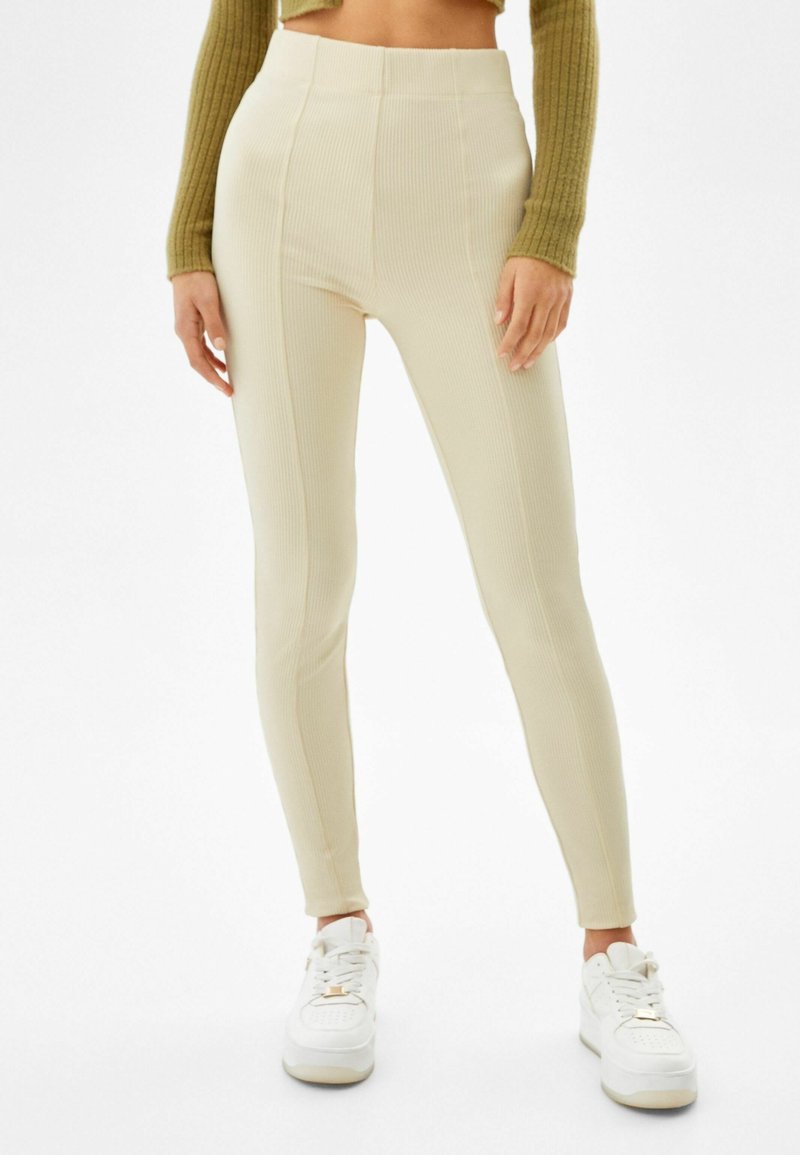 Leggings de tiro alto con canalé en color beige claro, confeccionados en un material elástico. Presenta una silueta ajustada y una textura suave. Combinados con zapatillas blancas.