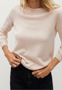 Helles rosa Strickpullover mit rundem Ausschnitt, langen Ärmeln und dezenten Nahtdetails. Weicher Stoff, kombiniert mit dunklen Jeans.