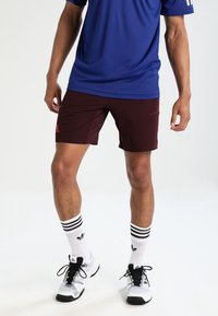 Bordeauxfärgade atletiska shorts med prickigt mönster, röd logotypdetalj, tillsammans med en blå t-shirt. Vita strumpor med svarta ränder och svarta sneakers.