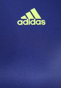 Navy blue tekstiili, millel on sile tekstuur, esitleb silmapaistvat helesinist Adidas logo ja kolme diagonaalset triipude mustrit.