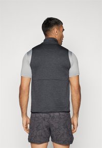 Gilet sans manches gris foncé avec un col haut, tissu texturé et conception ajustée. Associe avec un short gris à motifs.