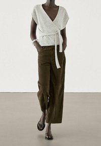 Light gray wrap top with short sleeves and a tied waist, paired with wide-leg olive green pants. Black flip-flops complete the outfit.