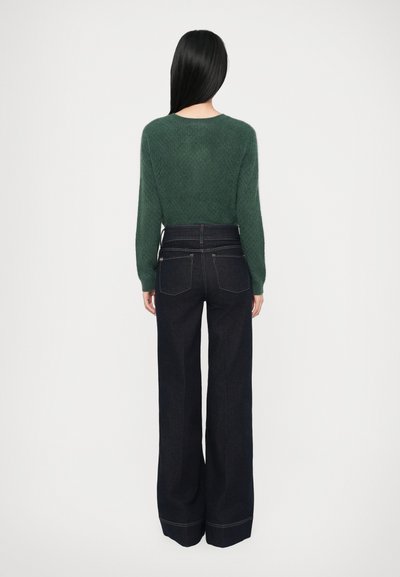 Green knit sweater with a textured finish paired with dark wash wide-leg jeans featuring contrast stitching and back pockets.