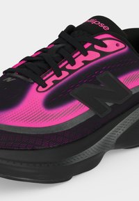 Baskets noires et rose vif avec lacets noirs, logo "N" noir sur le côté et accents métalliques gris sur la semelle intermédiaire.