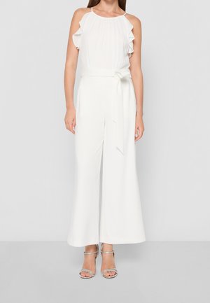 Valkoinen haalari, jossa röyhelöiset olkaimet, leveät lahkeet ja sidottava vyötärönauha. Yhdistetty hopeisiin remmikenkiin. Sileä kangaspinta.