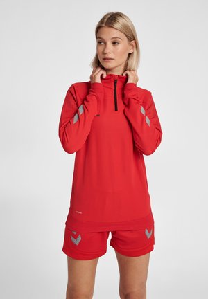 Rode sportoutfit met een lange mouwen ritsshirt met gestructureerde schouders en bijpassende shorts versierd met zilveren accenten.
