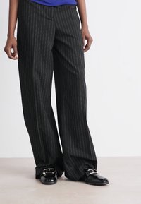 Striped wide-leg trousers in black with white pinstripes, made from smooth fabric. Features a high waist and flowing silhouette.