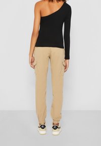 Mustat yhden olkapään toppi yhdistettynä vaaleanbeigeihin cargo-housuihin, joissa on sivutaskut, joustavat hihnat ja mustat lenkkarit valkoisilla pohjilla.