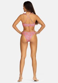 Różowy kostium kąpielowy w kwiaty składa się z falbaniastego biustonosza z krzyżującymi się ramiączkami oraz dopasowanych, wysokich majtek, wykonanych z teksturowanej tkaniny.