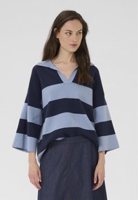 Pulover dungat albastru și marin cu dungi, cu decolteu în V și mâneci clopot. Material tricotat moale, cu o croială lejeră, asortat cu o fustă din denim.