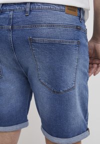 Tamne traperice s rolacijama u tamnoplavoj boji, s dva stražnja džepa i smešnom kožnom oznakom na struku, s teksturiranim i izblijedjelim izgledom.