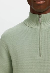 Mintgroene zip-up trui met hoge kraag; textuur breimateriaal; metalen ritssluiting detail bij de hals.