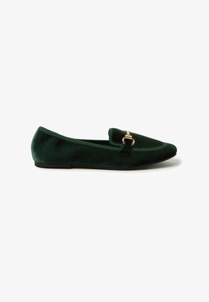Mocassino verde in velluto con punta affusolata, caratterizzato da una fibbia dorata sulla parte anteriore e una suola piatta nera. Texture morbida e design elegante.