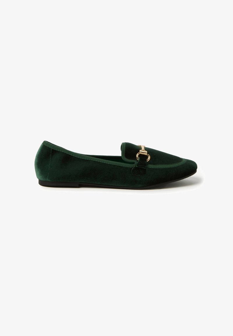 Mocasines de terciopelo verde con punta afilada, que cuentan con una hebilla dorada en la parte frontal y una suela negra plana. Textura suave y diseño elegante.