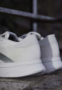 Ζευγάρι λευκά παπούτσια τρεξίματος Adidas με υφασμάτινη υφή και χονδρές σόλες σε λιθόστρωτο με θολό φόντο.