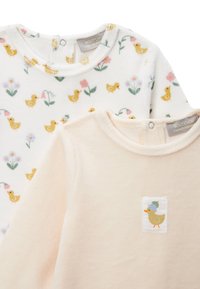 Deux petits hauts pour bébé : un blanc avec des canetons jaunes et des fleurs, l'autre pêche clair avec une application de canard. En tissu coton doux, avec des encolures rondes.