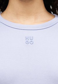 Ανοιχτό μωβ κοντομάνικο πουκάμισο με ριγέ υφή. Διαθέτει μικρό κεντημένο λογότυπο "HU GO" σε αντίστοιχο χρώμα στο στήθος.