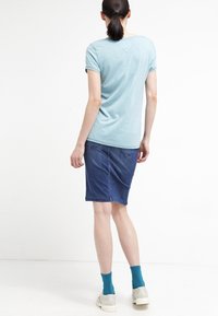 Ljusblå kortärmad t-shirt med rund halsringning, matchad med en åtsittande mörk denimkjol och grå snörskor, som bärs med turkosa strumpor.