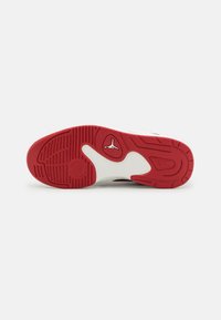 Scarpa sportiva rossa e bianca con suola in gomma testurizzata. Presenta un logo distintivo e un battistrada decorato per una migliore trazione. Design della punta arrotondata.