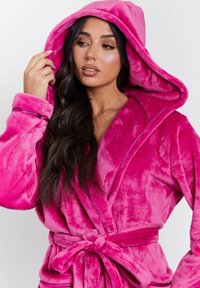 Accappatoio rosa in plush con cappuccio, maniche lunghe, cintura in vita e texture liscia. Presenta un profondo scollo a V e una fodera interna a contrasto.