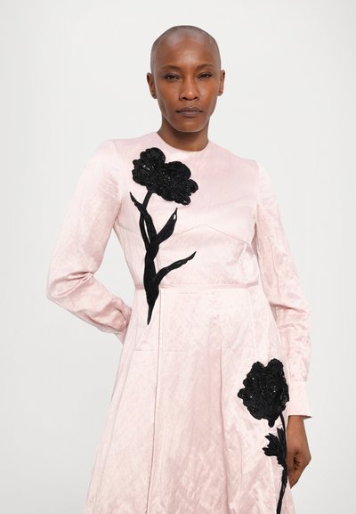 Long-sleeve pink dress with textured fabric, featuring black embroidered floral appliqués on the front and two side pockets.