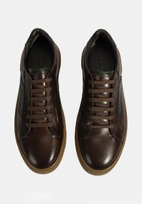 Braune Leder-Sneaker mit glatter Oberfläche, kontrastierenden grünen Akzenten und braunen Schnürsenkeln. Die Sohle besteht aus Gummi und ist leicht strukturiert.
