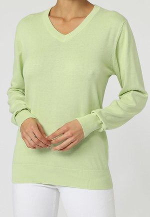 Suéter verde claro con cuello en V y mangas largas, hecho de un material de punto suave. Presenta puños y dobladillo acanalados, llevado sobre pantalones blancos.