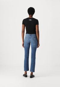 T-shirt nera aderente, maniche corte, con testo bianco sul retro. Jeans in denim blu, gamba dritta, lavaggio medio, decorazioni sottili sulle tasche posteriori.