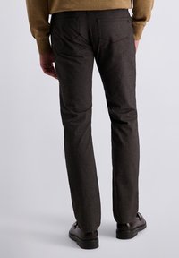 Pantalons marron texturés avec une coupe slim, dotés de poches arrière et de détails de coutures subtils. Associés à des chaussures noires.