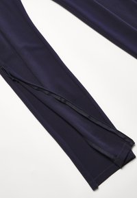 Navy blue athletic pants made from smooth fabric, featuring a side zippered opening and flatlock seams for added comfort.
