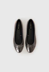 Pair of metallic gray ballet flats with front bows and black insoles branded Tommy Hilfiger, viewed from above on white background.