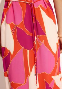 Sukienka z kwiatowym wzorem w odcieniach różu, pomarańczy i kremu, z wiązaniem w talii oraz gładką, lekką teksturą materiału.