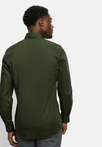 Donkergroen, lange mouwen shirt met een kraag. Heeft een gladde textuur en een getailleerde pasvorm, met knoopmanchetten en een gebogen zoom.