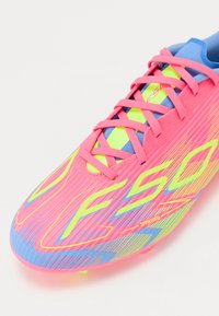 Ciorba de fotbal roz cu accente galbene strălucitoare, detalii albastre, suprafață texturată și șireturi subțiri. Prezintă un design aerodinamic și cuie modelate.