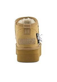 Stivaletto alla caviglia in velluto a coste color cammello con fodera in pelliccia sintetica bianca, suola piatta in gomma e un ciondolo decorativo argentato sul lato. Dotato di un pratico tirante sul retro.