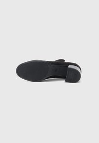 Scarpa nera in suede con tacco alto, suola in gomma texturizzata e un tacco robusto a blocco, caratterizzata da un design della punta liscio e arrotondato.