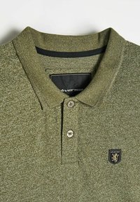 Oliwkowy podkoszulek polo z teksturowanej tkaniny, krótki kołnierzyk, zapięcie na dwa guziki oraz czarna naszywka z logo z wizerunkiem lwa.