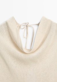 Haut en maille couleur crème avec un large col drapé et des liens fins noués dans le dos.