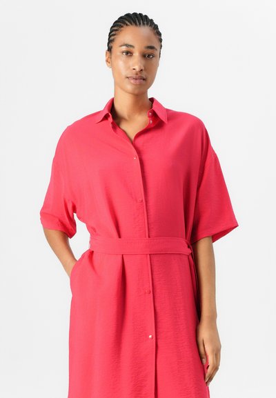 Robe chemise en tissu rose vif, avec un col, des manches courtes, une taille ceinturée et une coupe fluide avec des poches latérales.