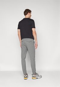 Light grey, textured pants with a tailored fit, paired with a black short-sleeve shirt and grey athletic footwear. Buttons on the back pockets.