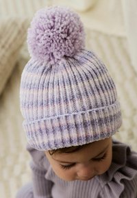 Lilla strikket hue med pom-pom, præget af lodrette ribber med pastelfarvede striber i lys lilla og blød pink. Behagelig tekstur.